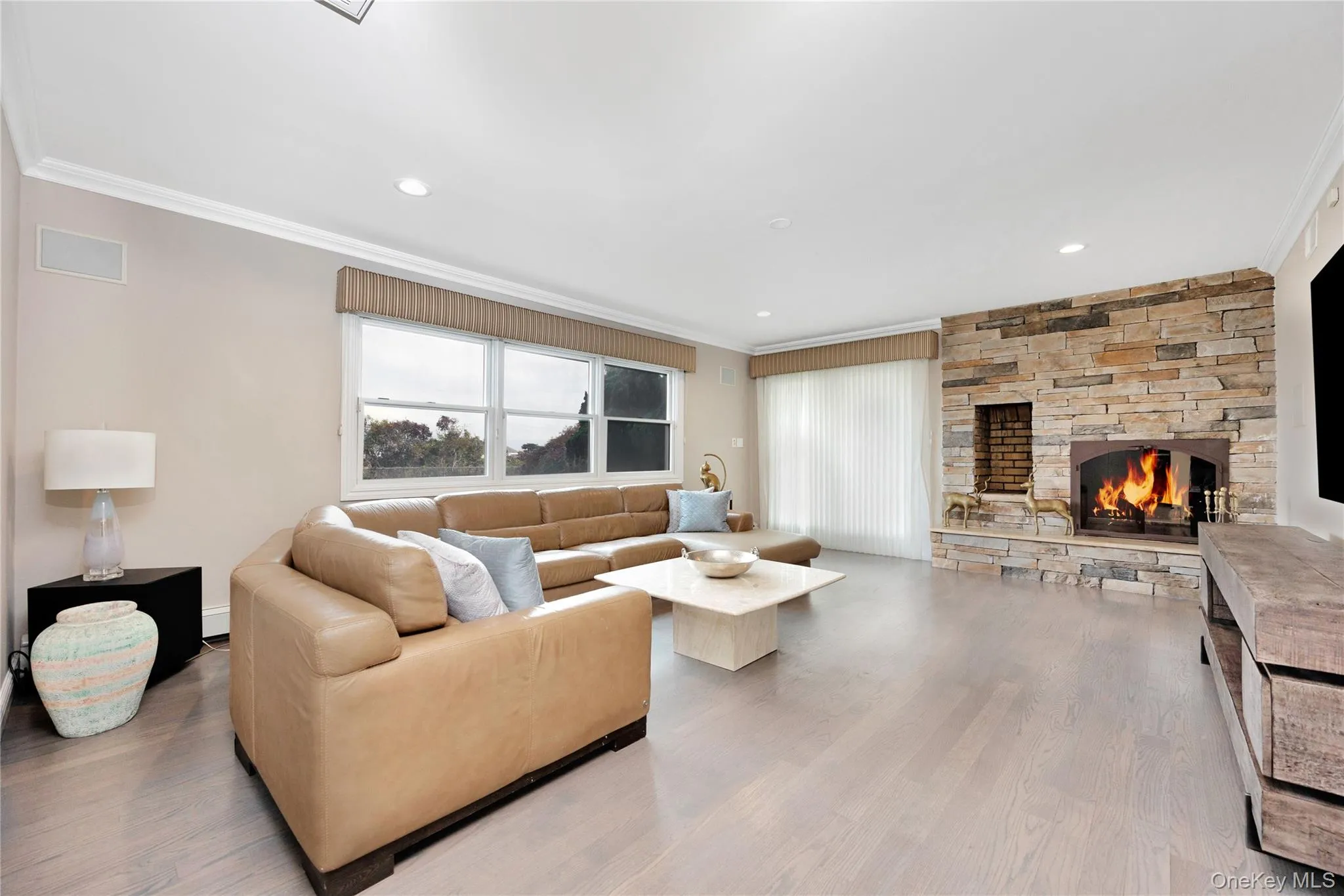 Living area with a stone fireplace, crown molding, light wood-style flooring, and recessed lighting Living area with a stone fireplace, crown molding, light wood-style flooring, and recessed lighting