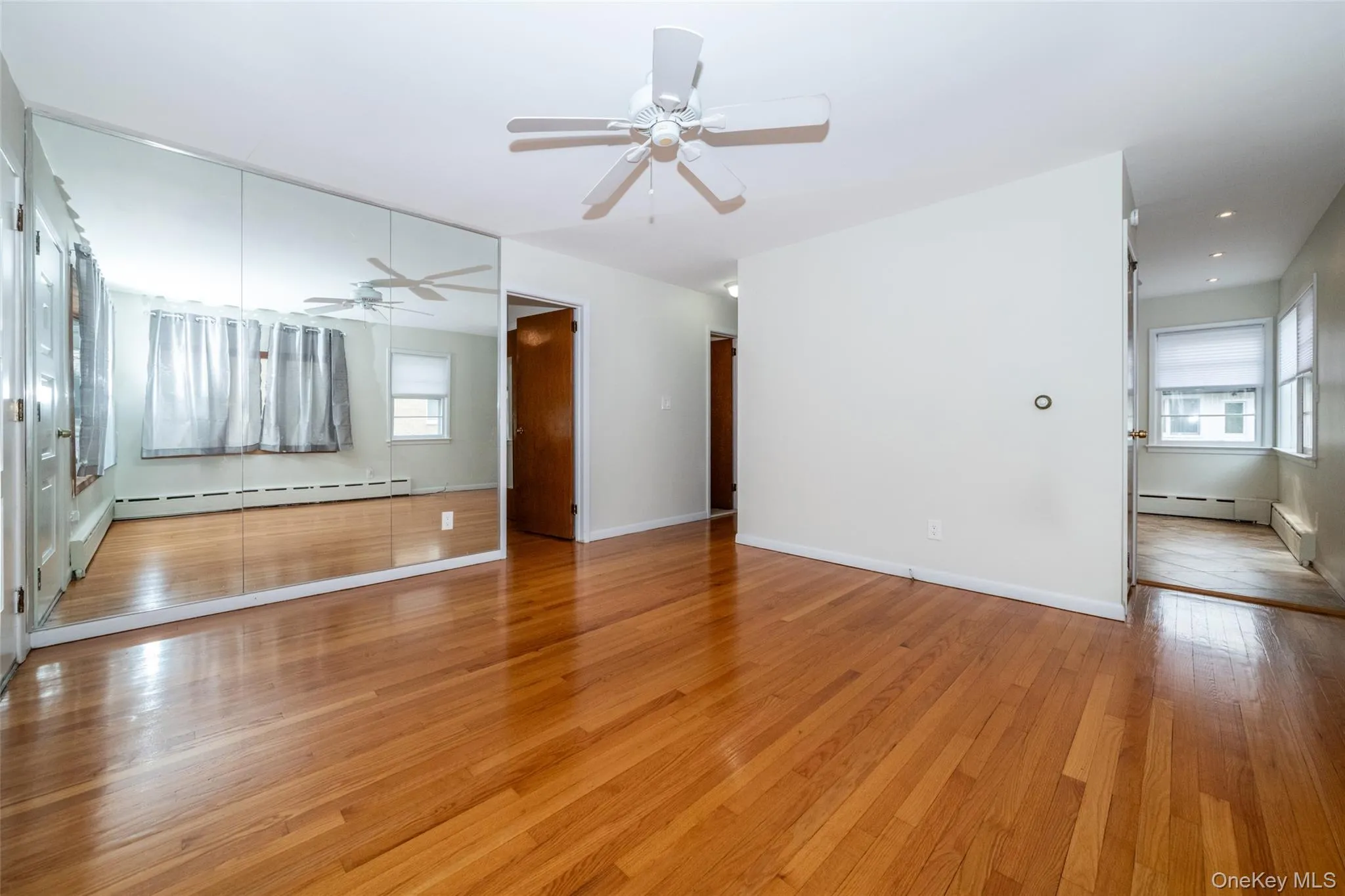 Unfurnished living room with light wood-type flooring, plenty of natural light, ceiling fan, and baseboard heating Unfurnished living room with light wood-type flooring, plenty of natural light, ceiling fan, and baseboard heating