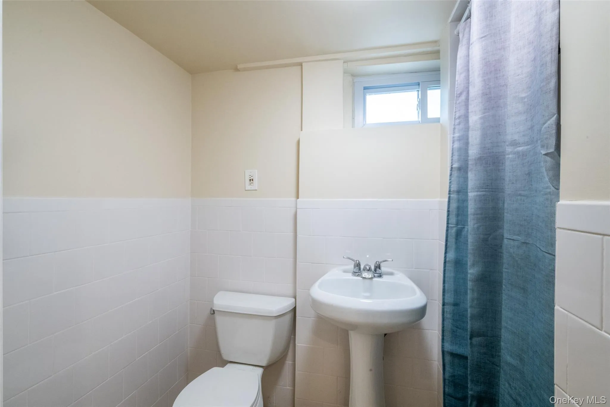 Full bath featuring wainscoting, a shower with shower curtain, and tile walls Full bath featuring wainscoting, a shower with shower curtain, and tile walls