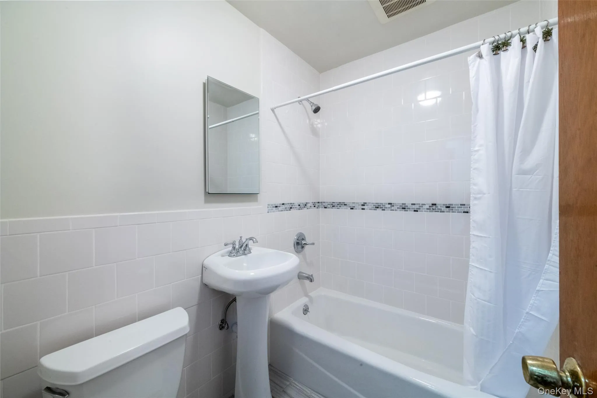 Full bathroom with tile walls, shower / tub combo with curtain, and wainscoting Full bathroom with tile walls, shower / tub combo with curtain, and wainscoting