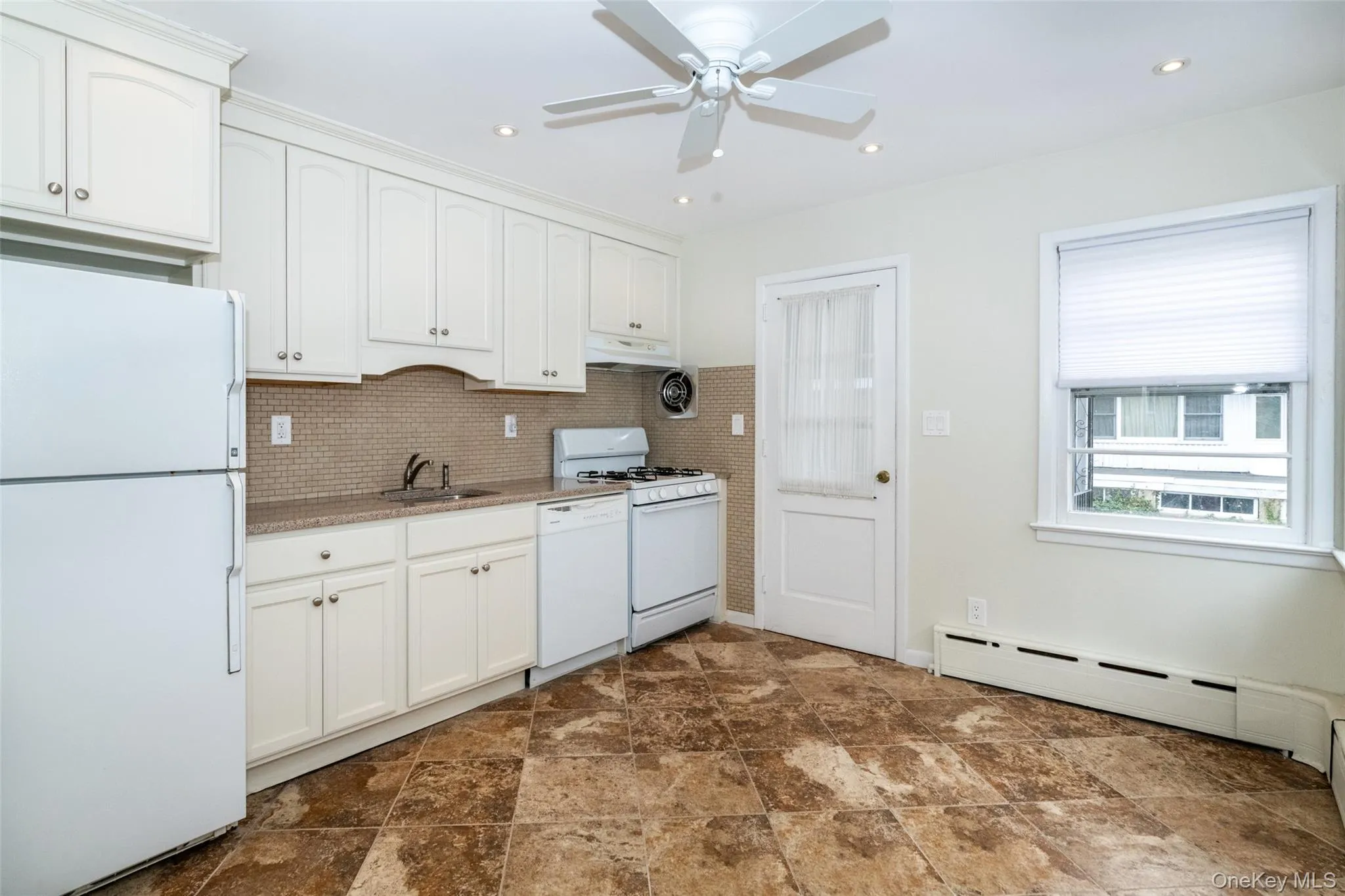 Kitchen with white appliances, white cabinetry, backsplash, under cabinet range hood, and recessed lighting Kitchen with white appliances, white cabinetry, backsplash, under cabinet range hood, and recessed lighting
