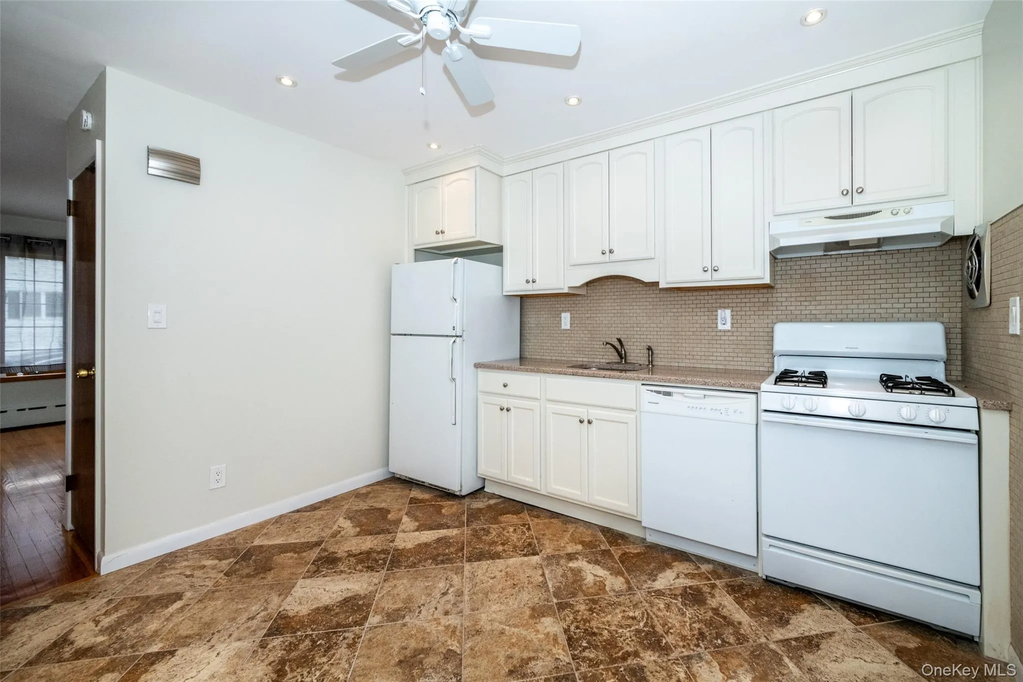 Kitchen with white appliances, under cabinet range hood, tasteful backsplash, stone finish flooring, and white cabinetry Kitchen with white appliances, under cabinet range hood, tasteful backsplash, stone finish flooring, and white cabinetry