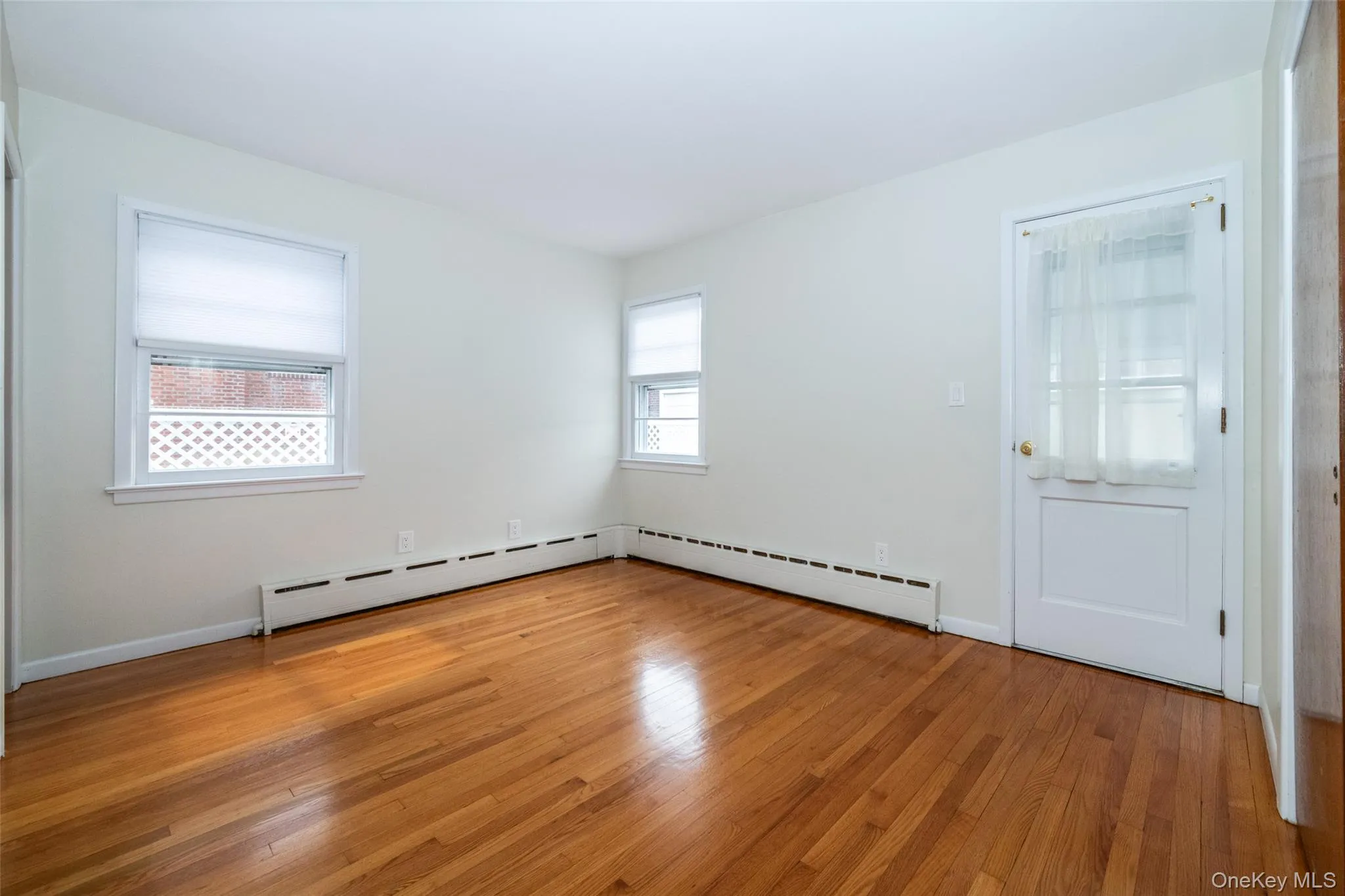 Unfurnished room featuring light wood-type flooring, a baseboard radiator, and a baseboard heating unit Unfurnished room featuring light wood-type flooring, a baseboard radiator, and a baseboard heating unit