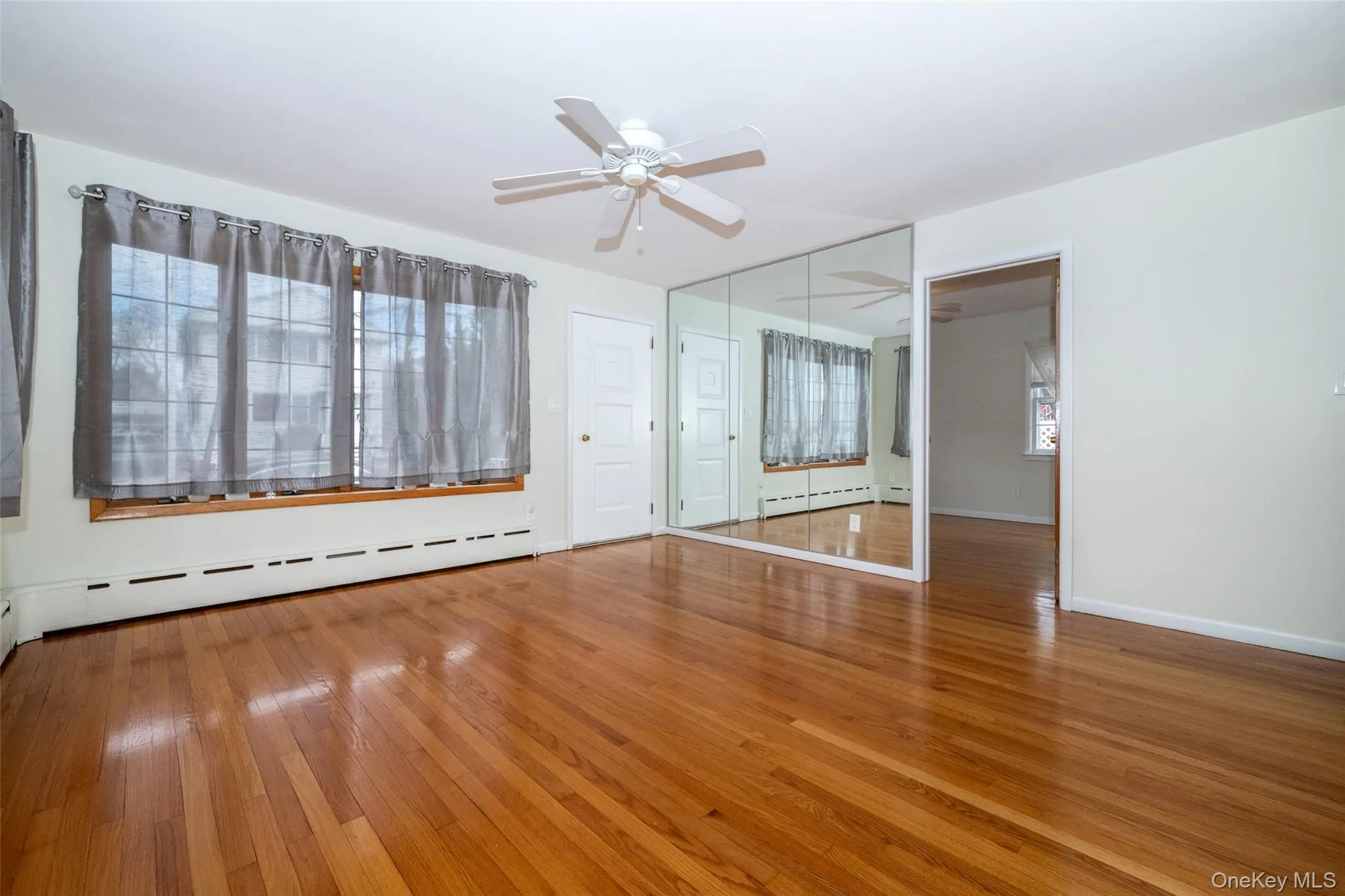 Unfurnished living room with light wood finished floors, baseboard heating, ceiling fan, and healthy amount of natural light Unfurnished living room with light wood finished floors, baseboard heating, ceiling fan, and healthy amount of natural light