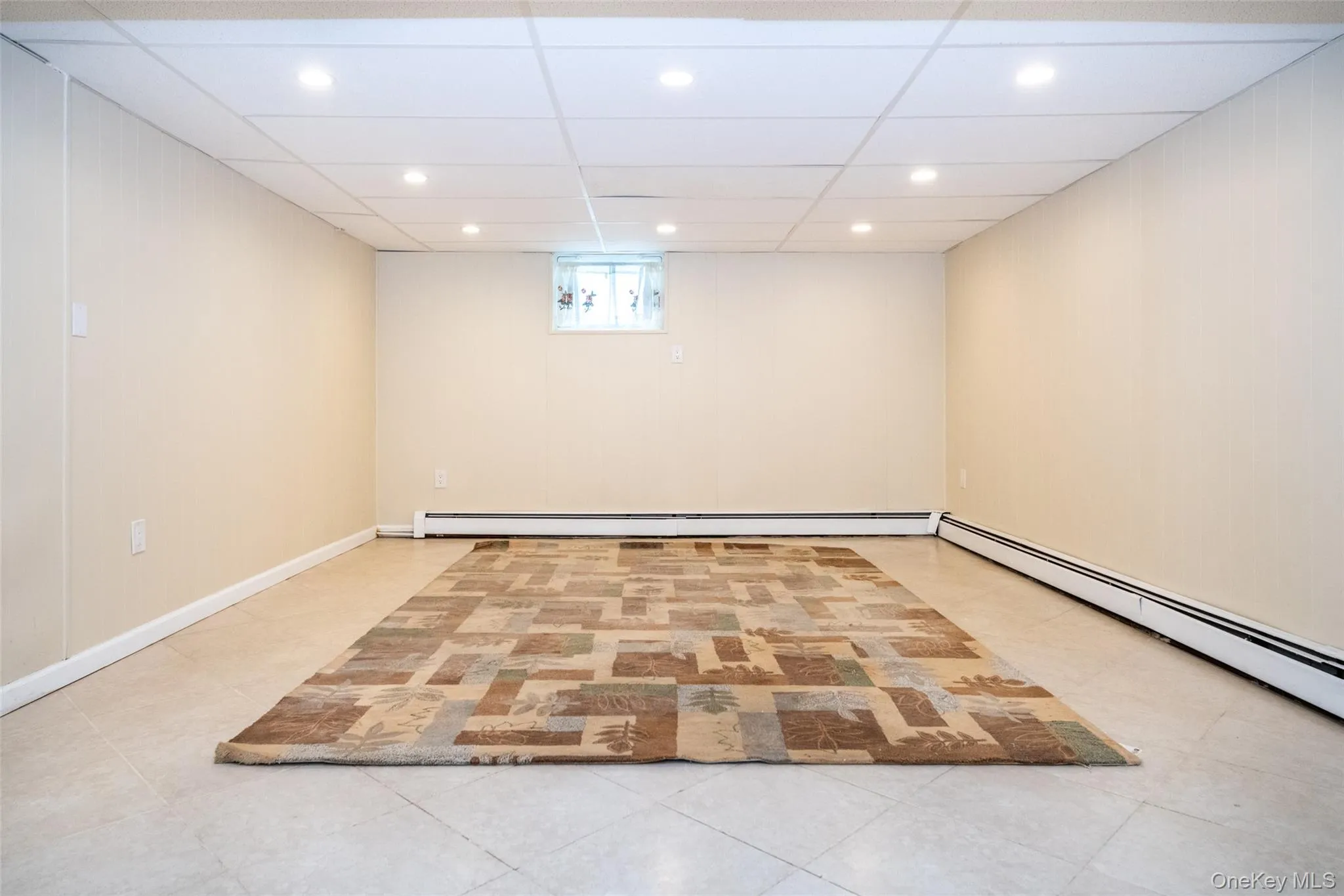 Below grade area featuring recessed lighting, light tile patterned floors, a paneled ceiling, and baseboard heating Below grade area featuring recessed lighting, light tile patterned floors, a paneled ceiling, and baseboard heating