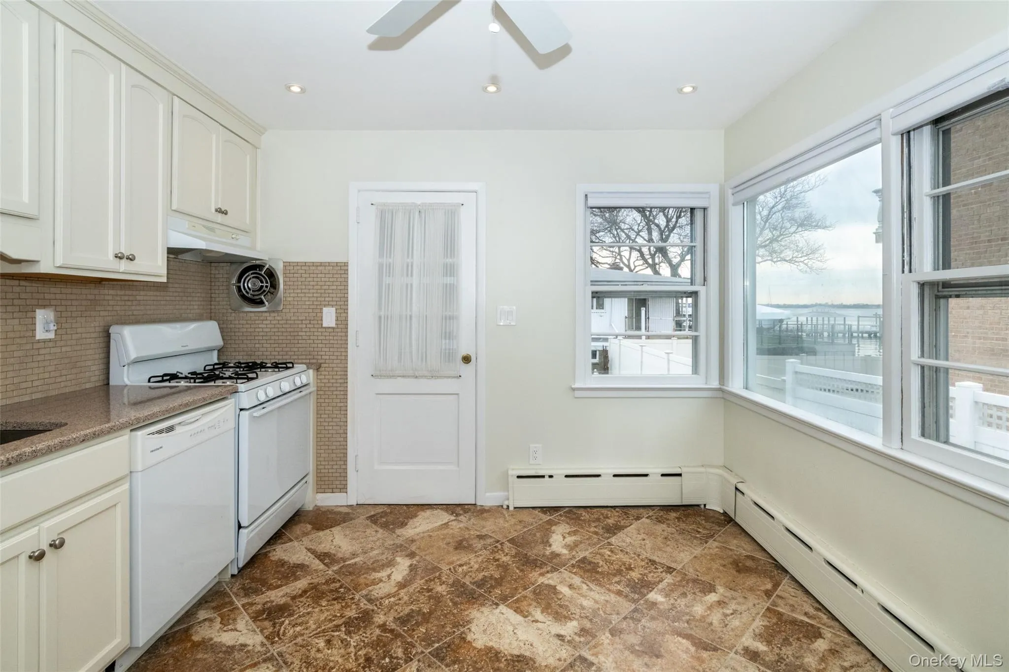 Kitchen featuring white appliances, baseboard heating, decorative backsplash, under cabinet range hood, and recessed lighting Kitchen featuring white appliances, baseboard heating, decorative backsplash, under cabinet range hood, and recessed lighting