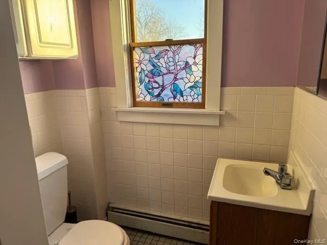 Bathroom featuring a baseboard heating unit, vanity, tile walls, and a wainscoted wall Bathroom featuring a baseboard heating unit, vanity, tile walls, and a wainscoted wall