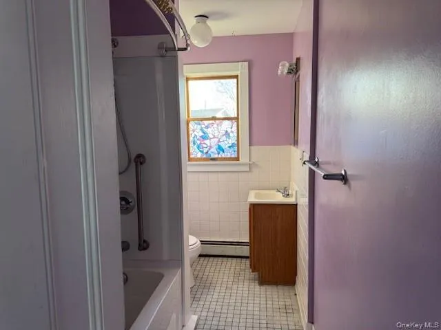 Bathroom with vanity, tile walls, a wainscoted wall, baseboard heating, and light tile patterned floors Bathroom with vanity, tile walls, a wainscoted wall, baseboard heating, and light tile patterned floors