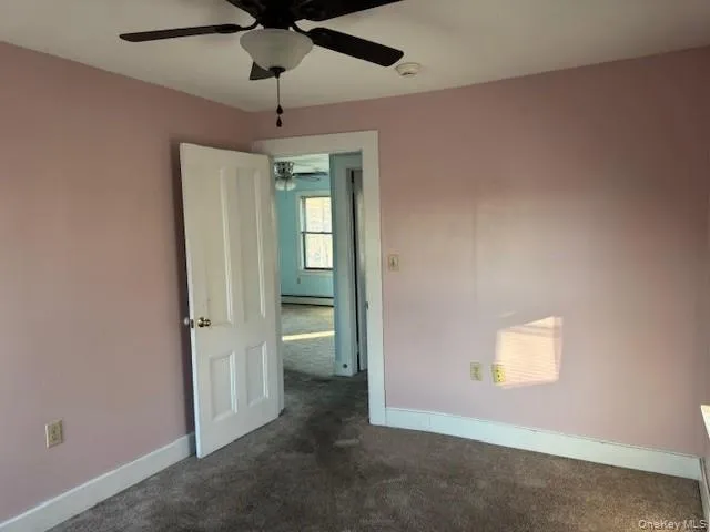 Bedroom featuring dark carpet, ceiling fan, and a baseboard heating unit Bedroom featuring dark carpet, ceiling fan, and a baseboard heating unit