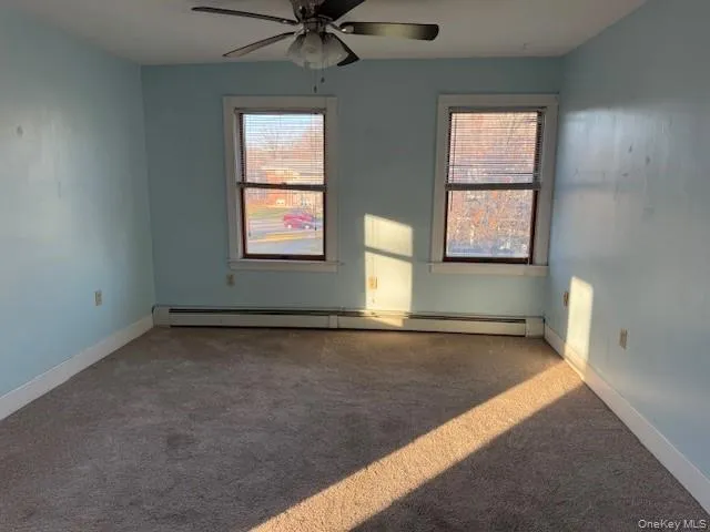 Living room with carpet floors, plenty of natural light, baseboard heating, and a ceiling fan Living room with carpet floors, plenty of natural light, baseboard heating, and a ceiling fan