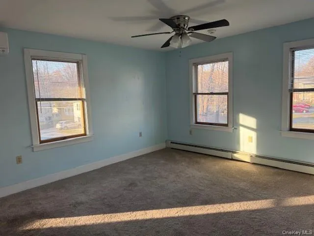 Carpeted Living room with a baseboard heating unit, plenty of natural light, an AC wall unit, and ceiling fan Carpeted Living room with a baseboard heating unit, plenty of natural light, an AC wall unit, and ceiling fan