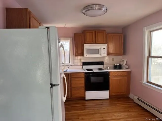 Kitchen with white appliances, a baseboard radiator, light countertops, brown cabinetry, and dark wood finished floors Kitchen with white appliances, a baseboard radiator, light countertops, brown cabinetry, and dark wood finished floors
