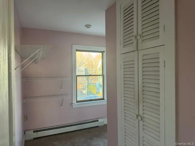 Walk in closet with a baseboard radiator and dark colored carpet Walk in closet with a baseboard radiator and dark colored carpet