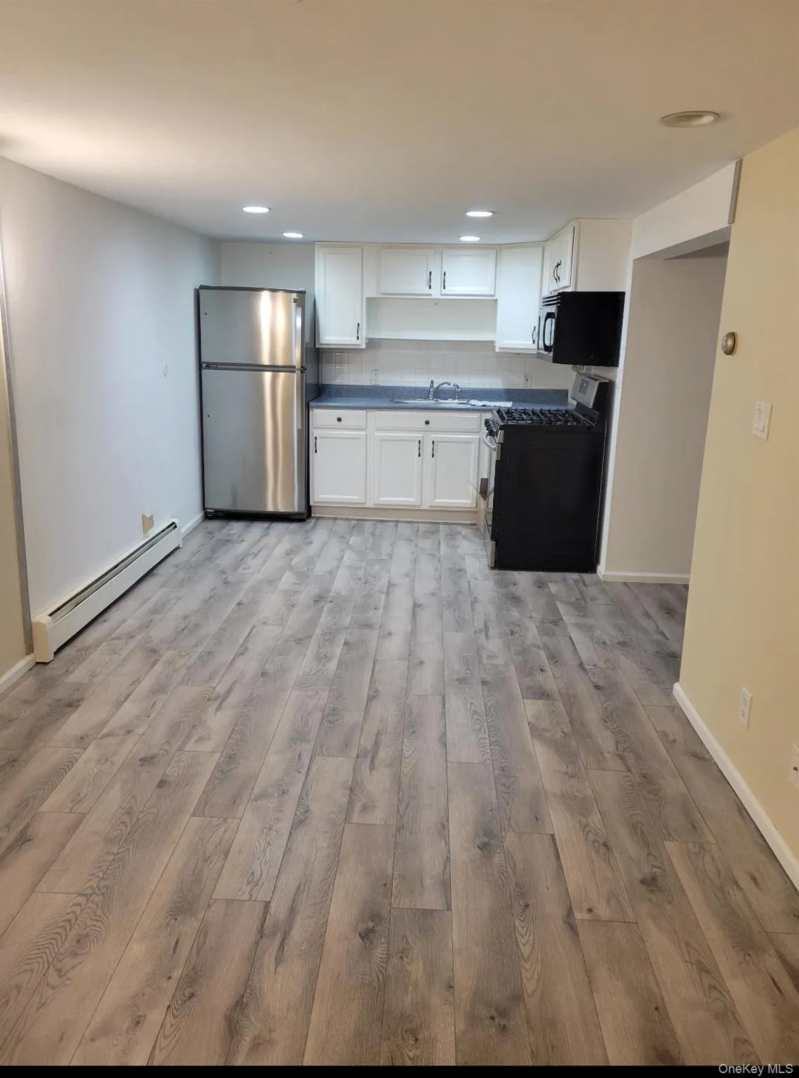 Kitchen with baseboard heating, stainless steel appliances, white cabinetry, open shelves, and dark countertops Kitchen with baseboard heating, stainless steel appliances, white cabinetry, open shelves, and dark countertops