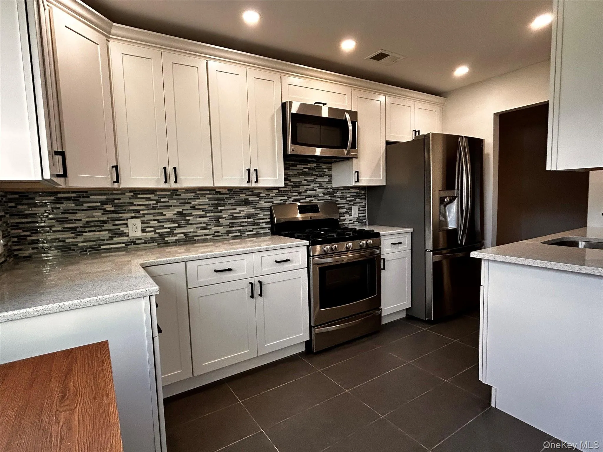 Kitchen featuring appliances with stainless steel finishes, light stone counters, tasteful backsplash, dark tile patterned flooring, and white cabinetry Kitchen featuring appliances with stainless steel finishes, light stone counters, tasteful backsplash, dark tile patterned flooring, and white cabinetry