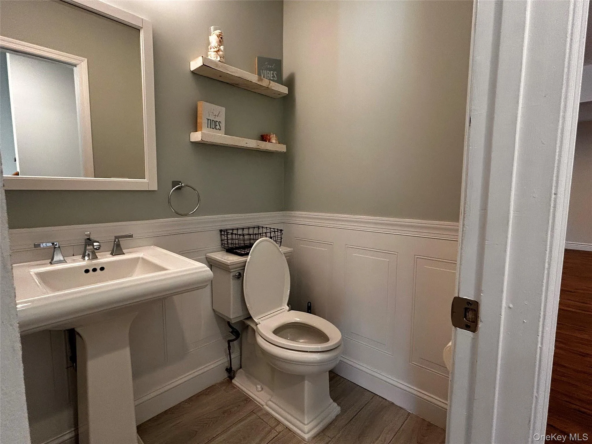 Bathroom featuring light wood-type flooring, wainscoting, and a decorative wall Bathroom featuring light wood-type flooring, wainscoting, and a decorative wall