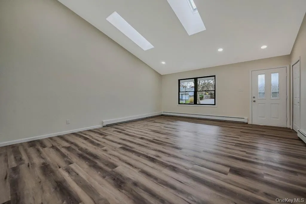 Living room with new Luxury Vinyl floors, a baseboard heating unit, recessed lighting, high vaulted ceiling, and a skylight Living room with new Luxury Vinyl floors, a baseboard heating unit, recessed lighting, high vaulted ceiling, and a skylight
