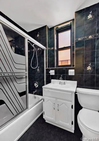 Bathroom featuring shower / bath combination with glass door, tile walls, and vanity Bathroom featuring shower / bath combination with glass door, tile walls, and vanity