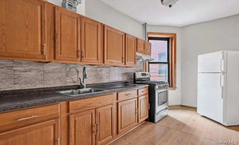 Kitchen with freestanding refrigerator, backsplash, dark countertops, and stainless steel range with gas cooktop Kitchen with freestanding refrigerator, backsplash, dark countertops, and stainless steel range with gas cooktop