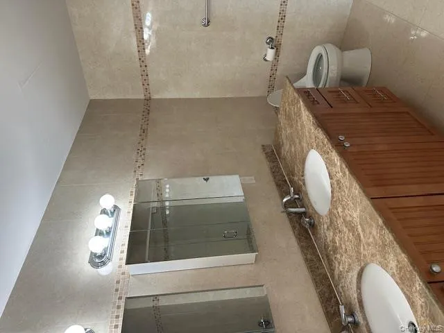 Bathroom featuring tile walls, double vanity, light tile patterned floors, and a shower stall Bathroom featuring tile walls, double vanity, light tile patterned floors, and a shower stall