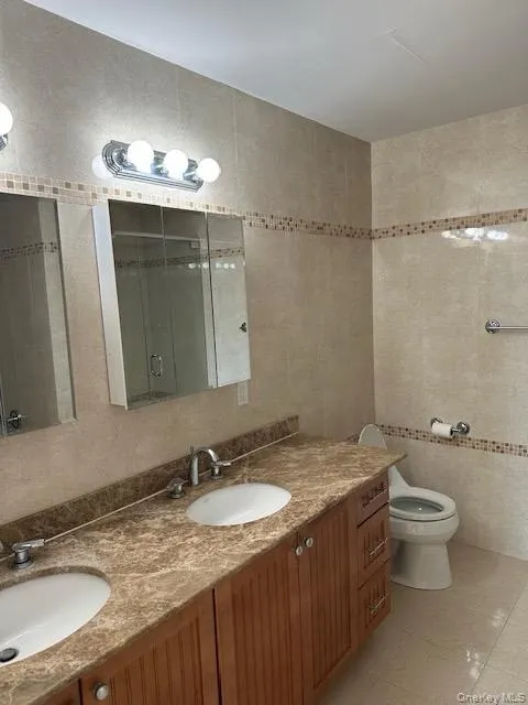 Full bathroom featuring double vanity, tile walls, light tile patterned floors, and a shower stall Full bathroom featuring double vanity, tile walls, light tile patterned floors, and a shower stall