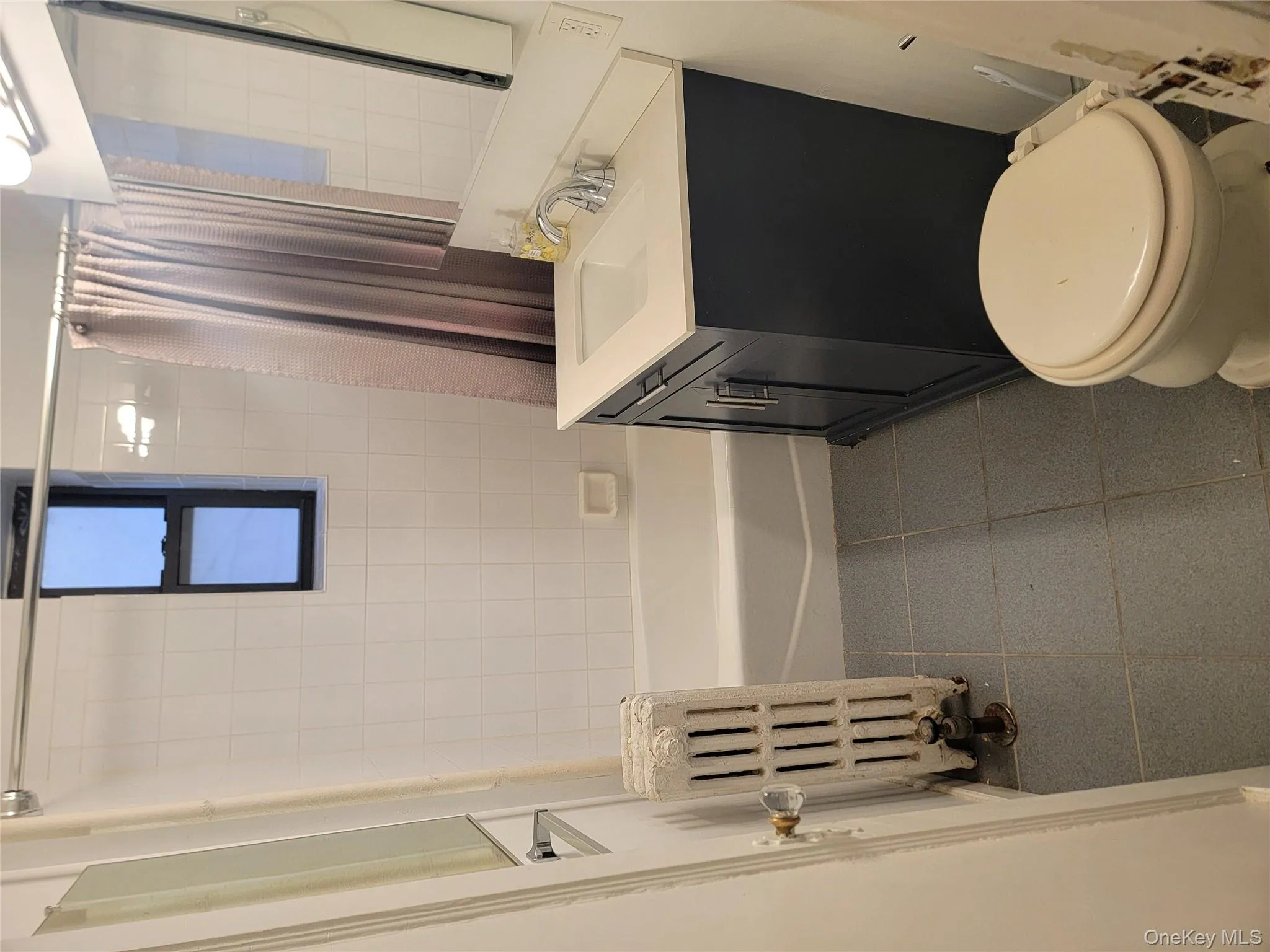 Full bath featuring vanity, radiator heating unit, shower / bath combo with shower curtain, and dark tile patterned floors Full bath featuring vanity, radiator heating unit, shower / bath combo with shower curtain, and dark tile patterned floors