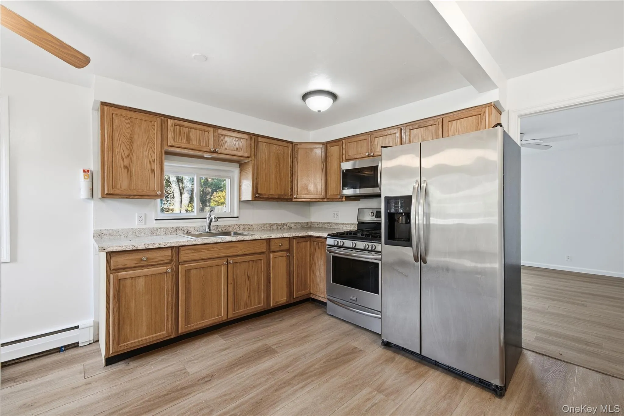 Kitchen featuring appliances with stainless steel finishes, brown cabinets, light wood-style flooring, and a baseboard radiator Kitchen featuring appliances with stainless steel finishes, brown cabinets, light wood-style flooring, and a baseboard radiator