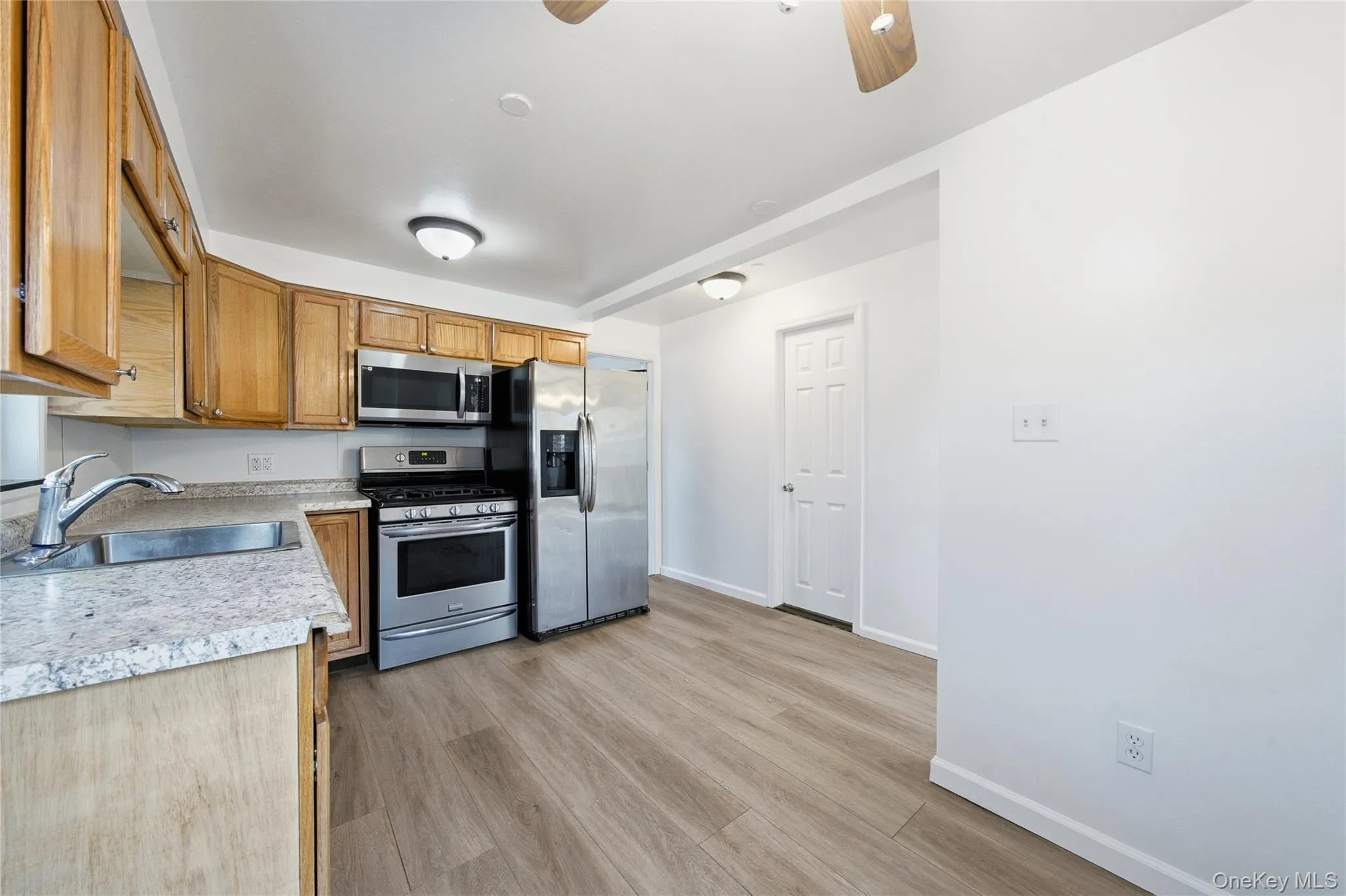 Kitchen featuring light countertops, appliances with stainless steel finishes, brown cabinetry, light wood-type flooring, and a ceiling fan Kitchen featuring light countertops, appliances with stainless steel finishes, brown cabinetry, light wood-type flooring, and a ceiling fan