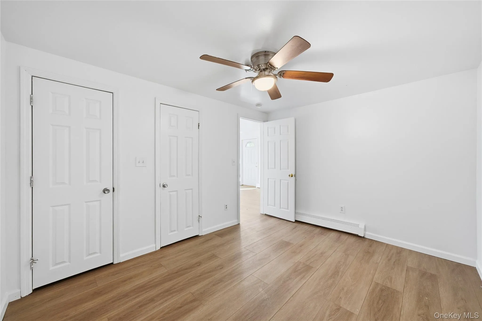 Unfurnished bedroom featuring light wood-type flooring, two closets, baseboard heating, and ceiling fan Unfurnished bedroom featuring light wood-type flooring, two closets, baseboard heating, and ceiling fan