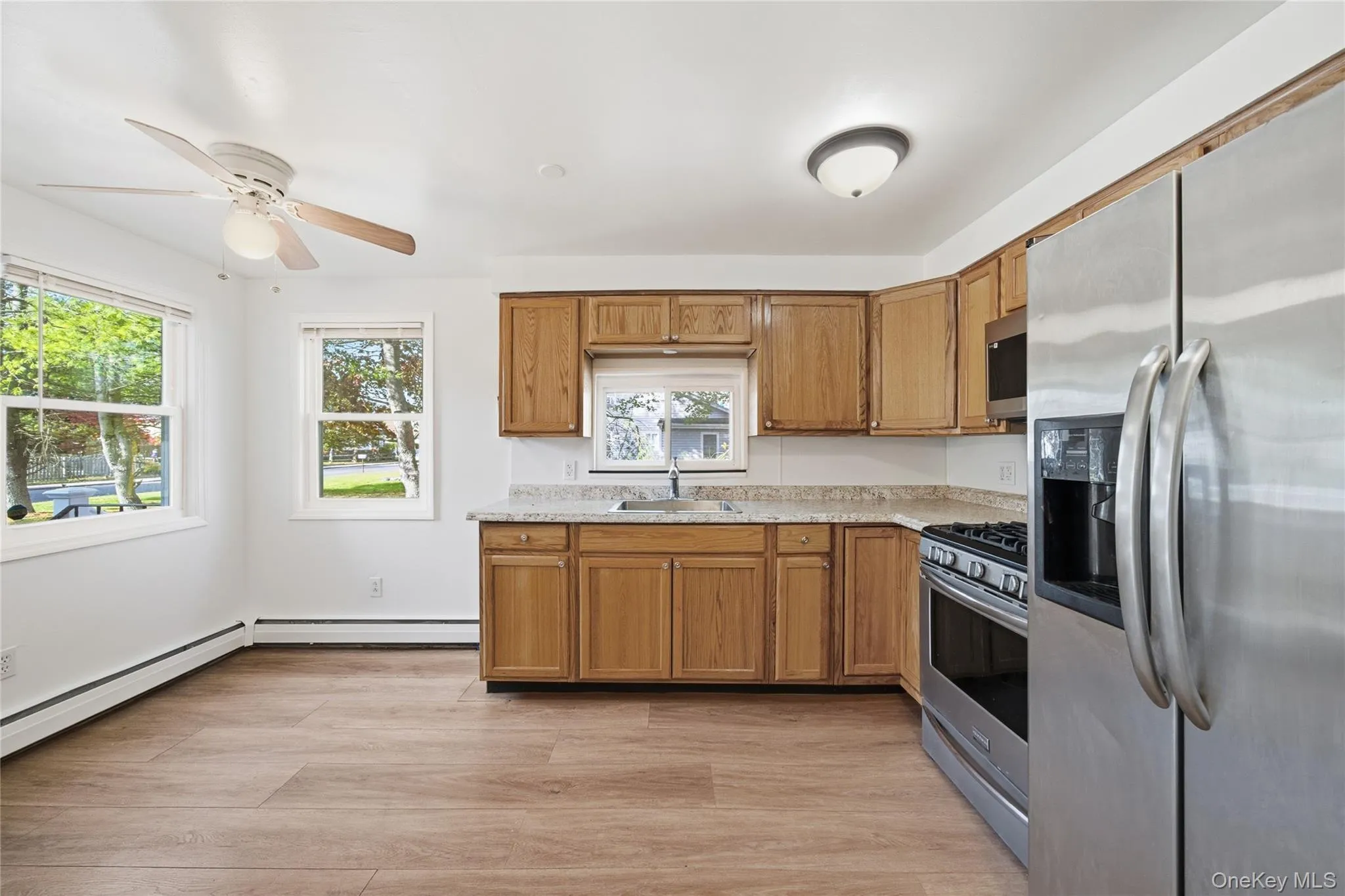 Kitchen with appliances with stainless steel finishes, brown cabinets, light wood finished floors, ceiling fan, and baseboard heating Kitchen with appliances with stainless steel finishes, brown cabinets, light wood finished floors, ceiling fan, and baseboard heating