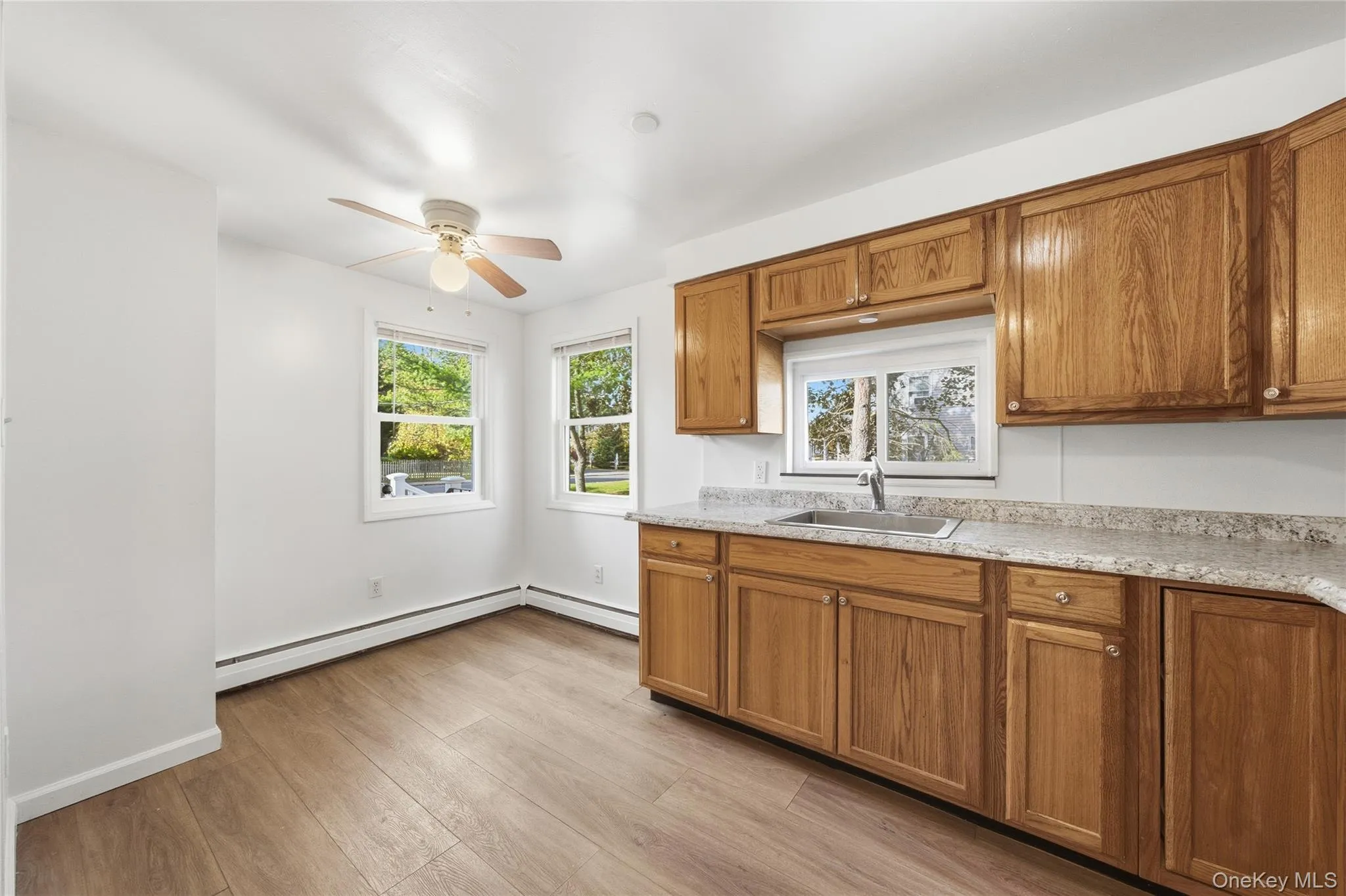 Kitchen with brown cabinetry, light wood-style flooring, a ceiling fan, and baseboard heating Kitchen with brown cabinetry, light wood-style flooring, a ceiling fan, and baseboard heating