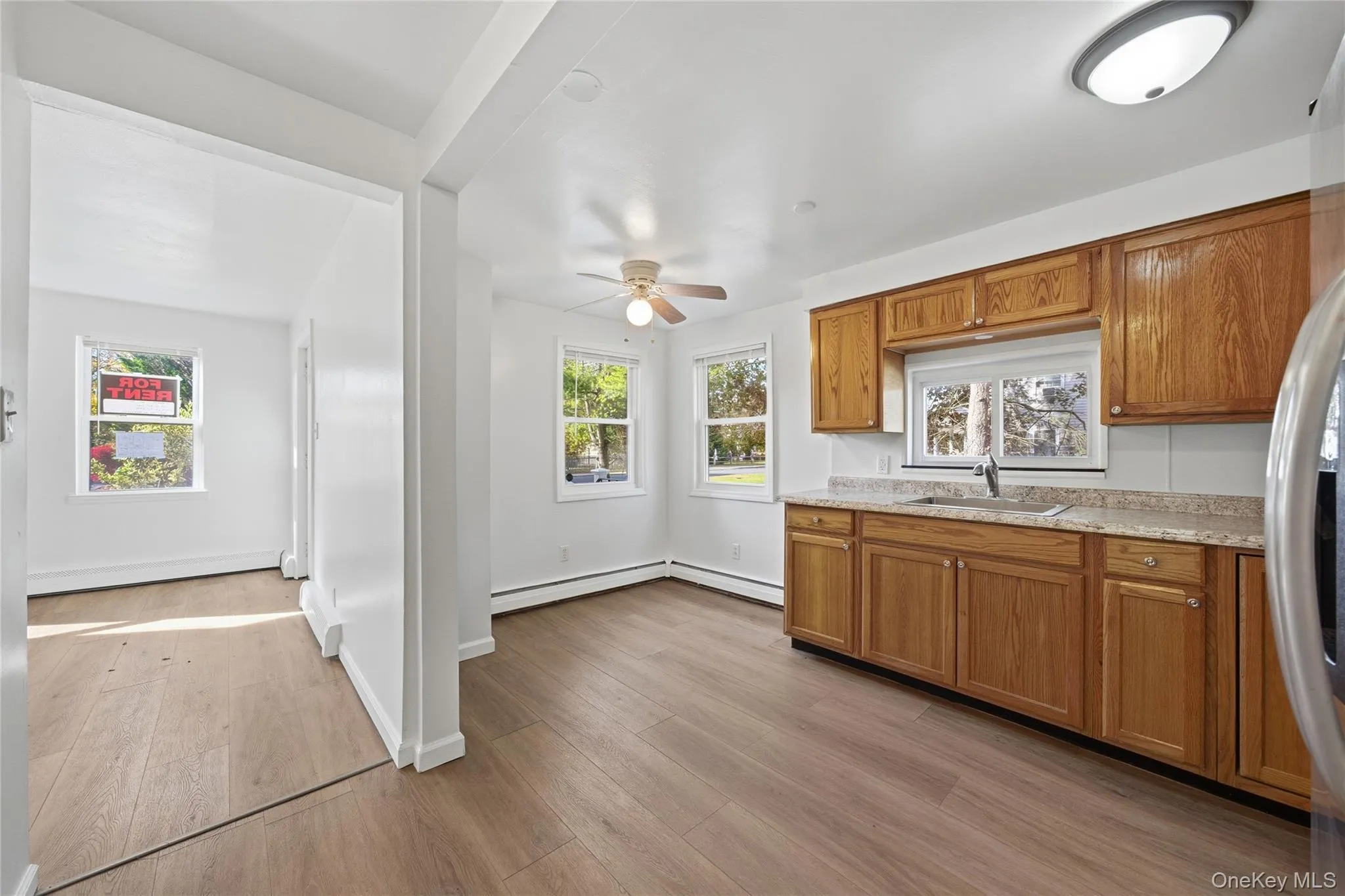 Kitchen featuring brown cabinets, light wood-type flooring, freestanding refrigerator, ceiling fan, and a baseboard radiator Kitchen featuring brown cabinets, light wood-type flooring, freestanding refrigerator, ceiling fan, and a baseboard radiator