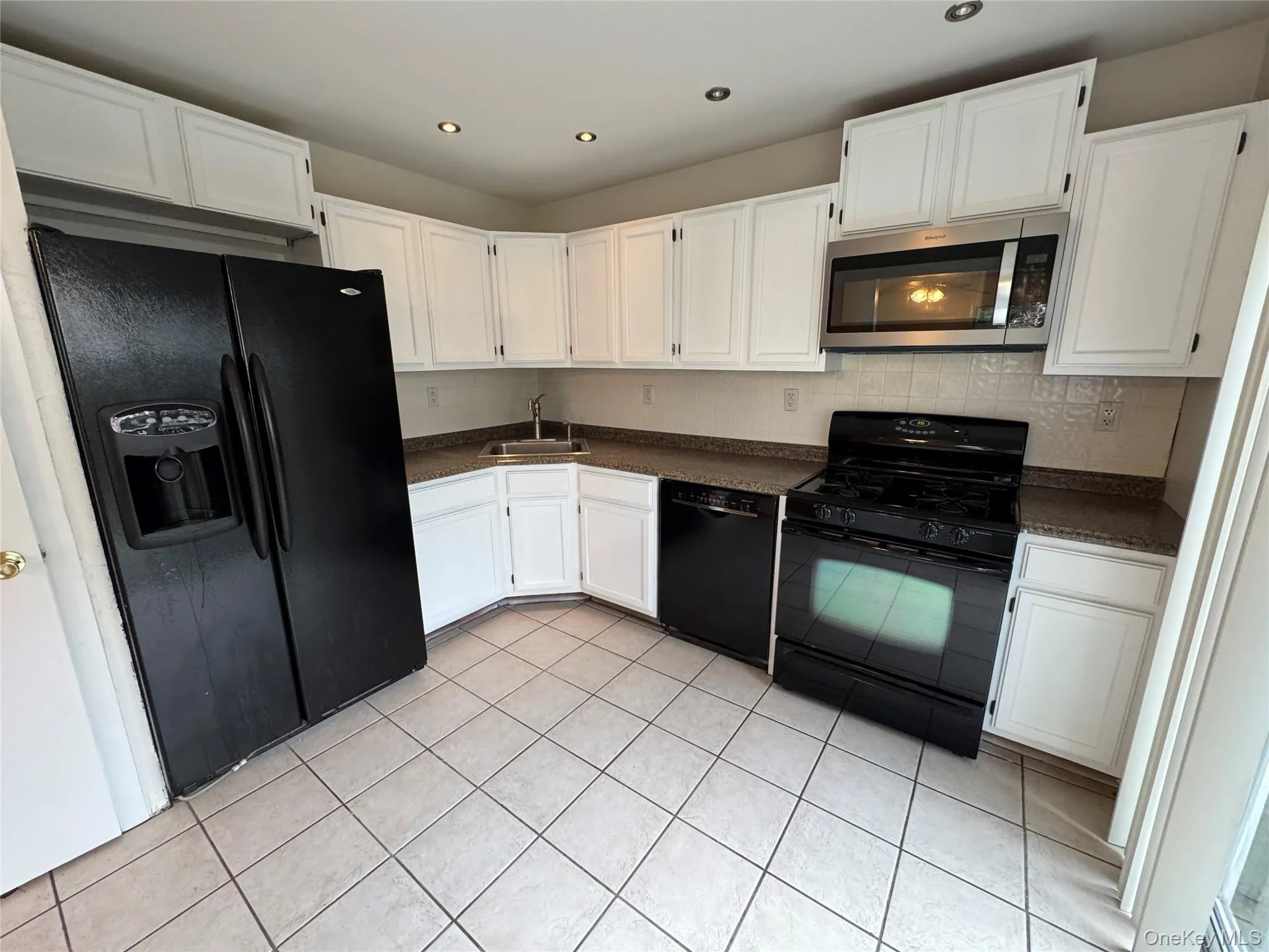 Kitchen featuring dark countertops, black appliances, white cabinetry, light tile patterned floors, and recessed lighting Kitchen featuring dark countertops, black appliances, white cabinetry, light tile patterned floors, and recessed lighting