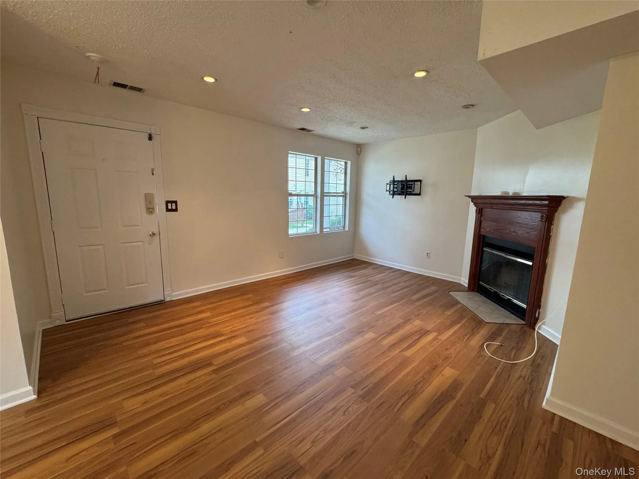 Unfurnished living room with a textured ceiling, a fireplace with flush hearth, light wood-style floors, and recessed lighting Unfurnished living room with a textured ceiling, a fireplace with flush hearth, light wood-style floors, and recessed lighting
