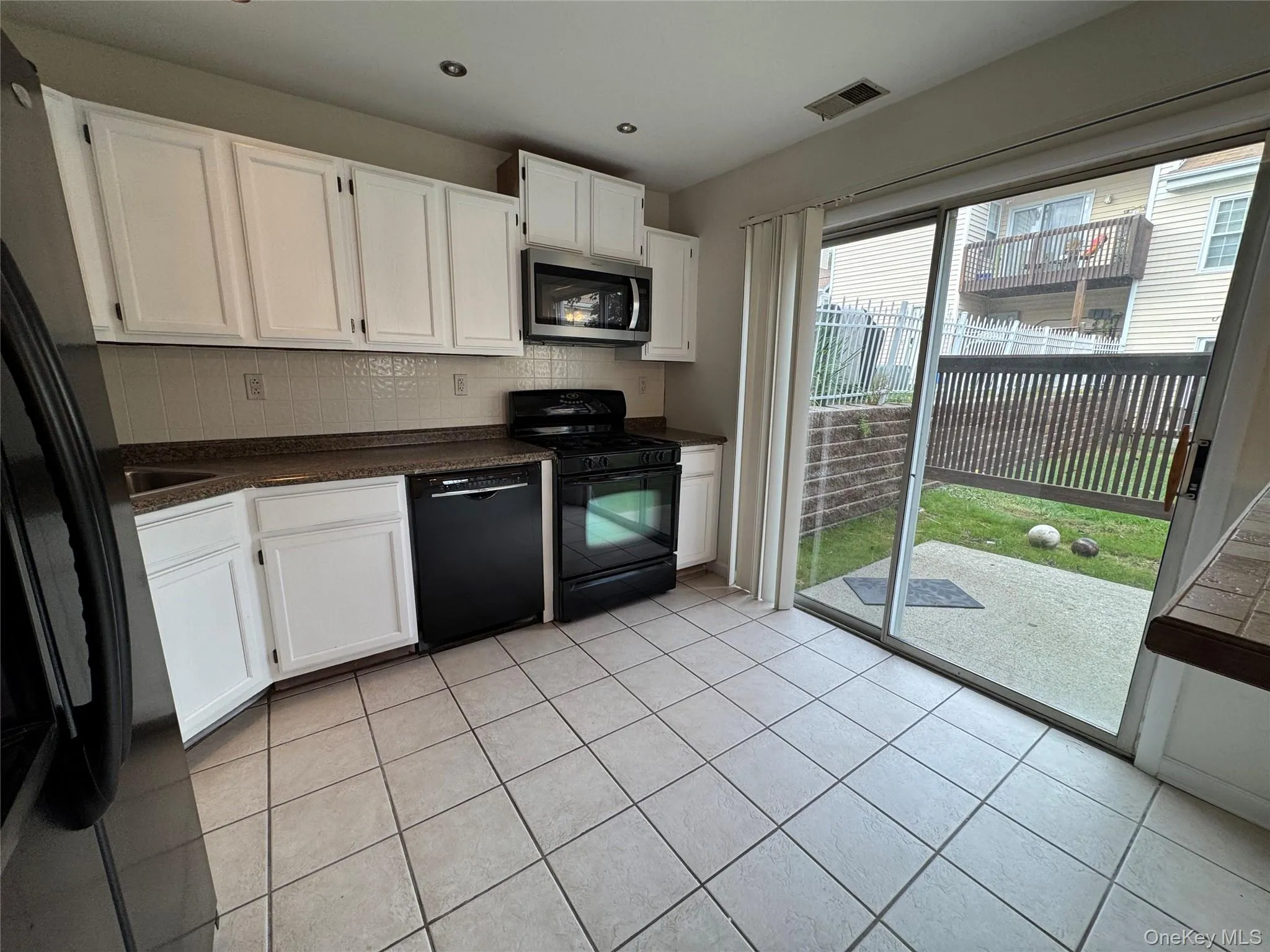 Kitchen with white cabinetry, decorative backsplash, black appliances, dark countertops, and light tile patterned floors Kitchen with white cabinetry, decorative backsplash, black appliances, dark countertops, and light tile patterned floors
