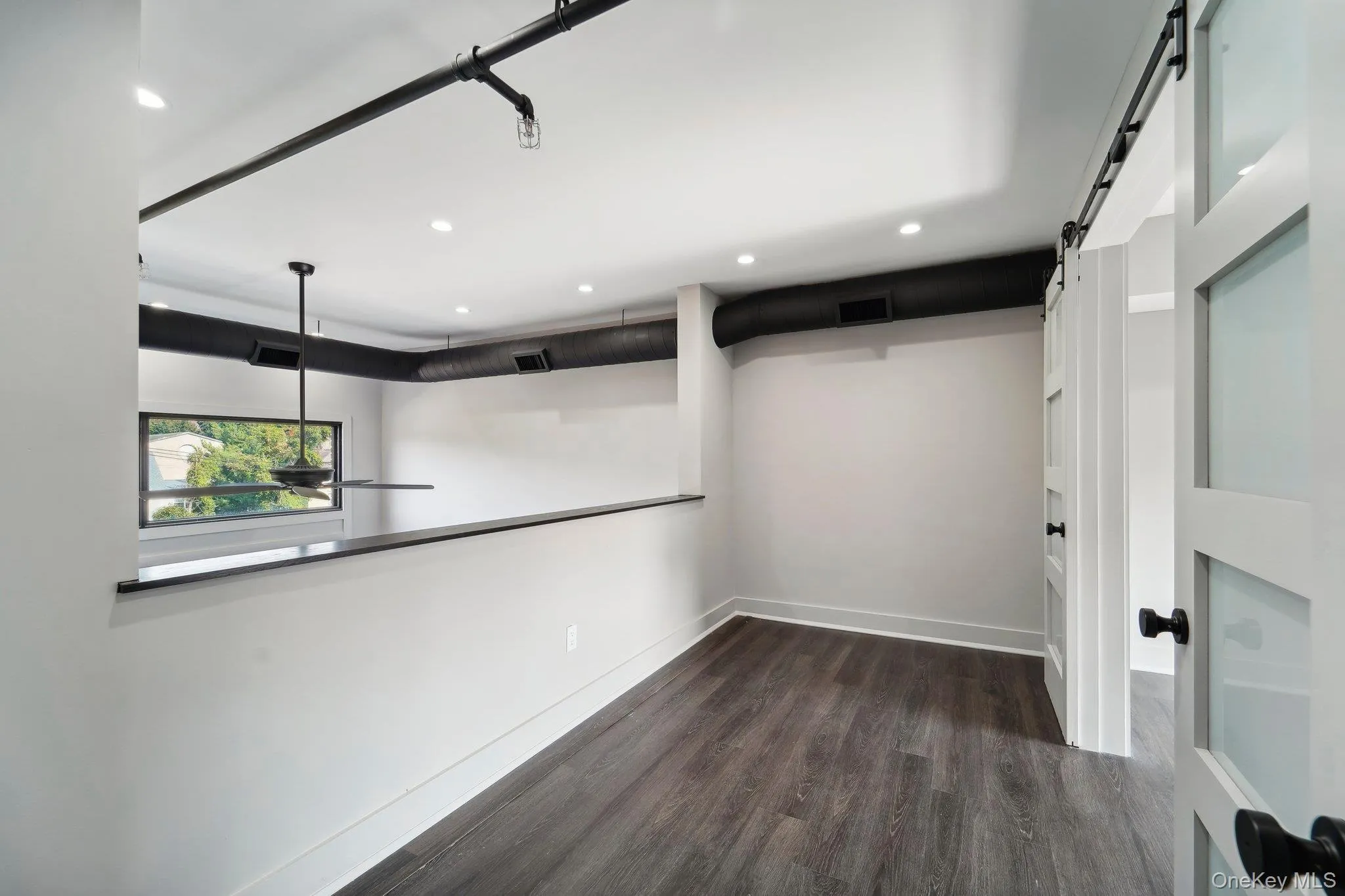 Unfurnished room with a barn door, recessed lighting, and dark wood-style flooring Unfurnished room with a barn door, recessed lighting, and dark wood-style flooring