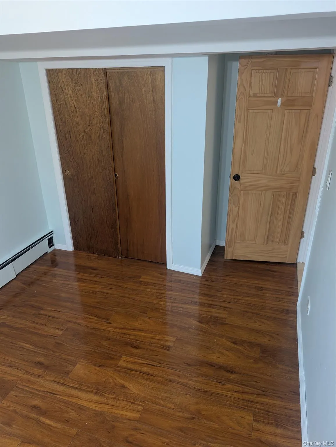 Unfurnished bedroom featuring a baseboard heating unit, dark wood-type flooring, and a closet Unfurnished bedroom featuring a baseboard heating unit, dark wood-type flooring, and a closet