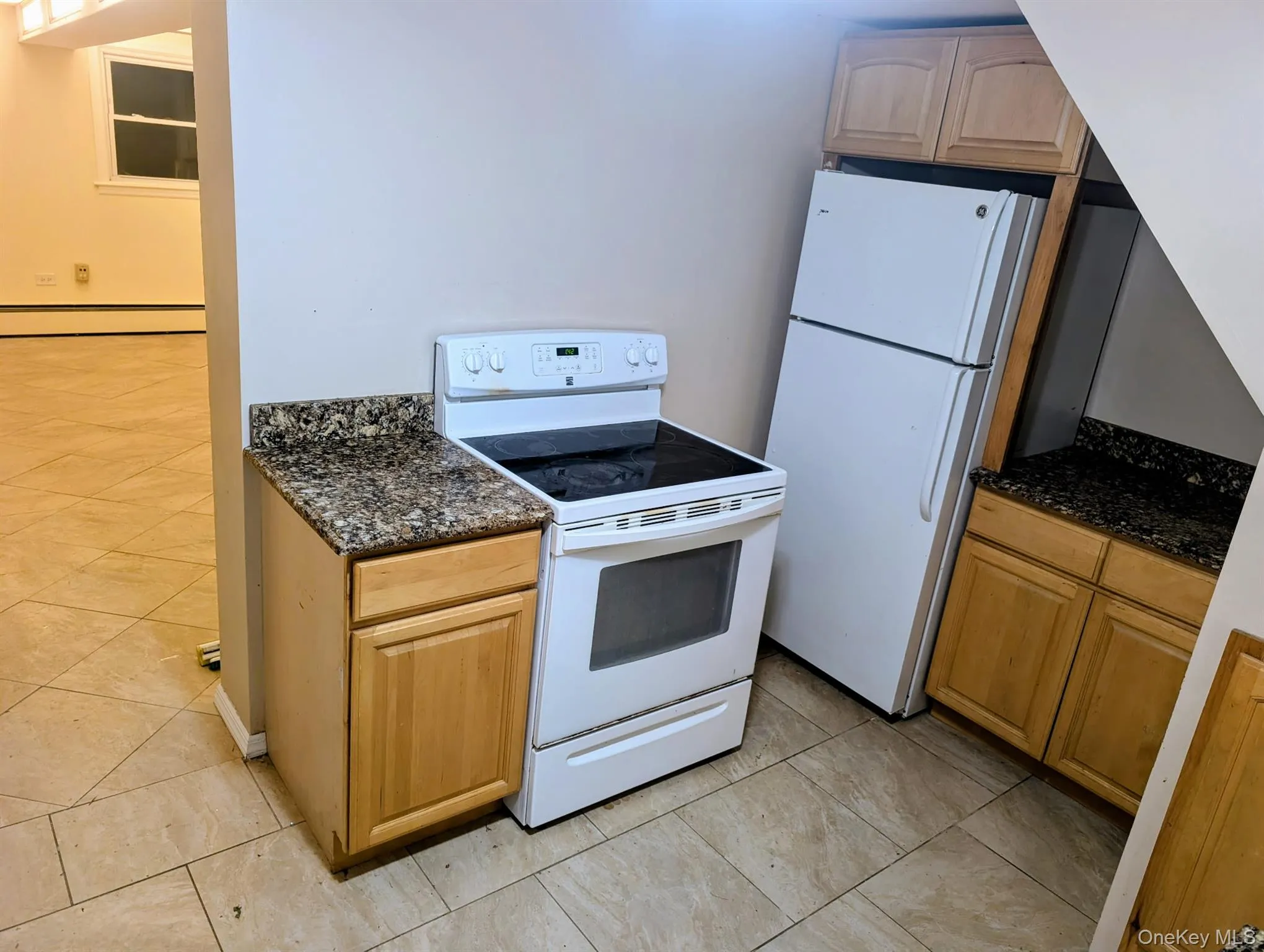 Kitchen with white appliances, dark stone counters, light tile patterned floors, and a baseboard radiator Kitchen with white appliances, dark stone counters, light tile patterned floors, and a baseboard radiator