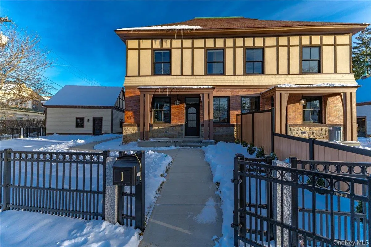 Tudor home featuring a gate, a fenced front yard, covered porch, brick siding, and stone siding Tudor home featuring a gate, a fenced front yard, covered porch, brick siding, and stone siding