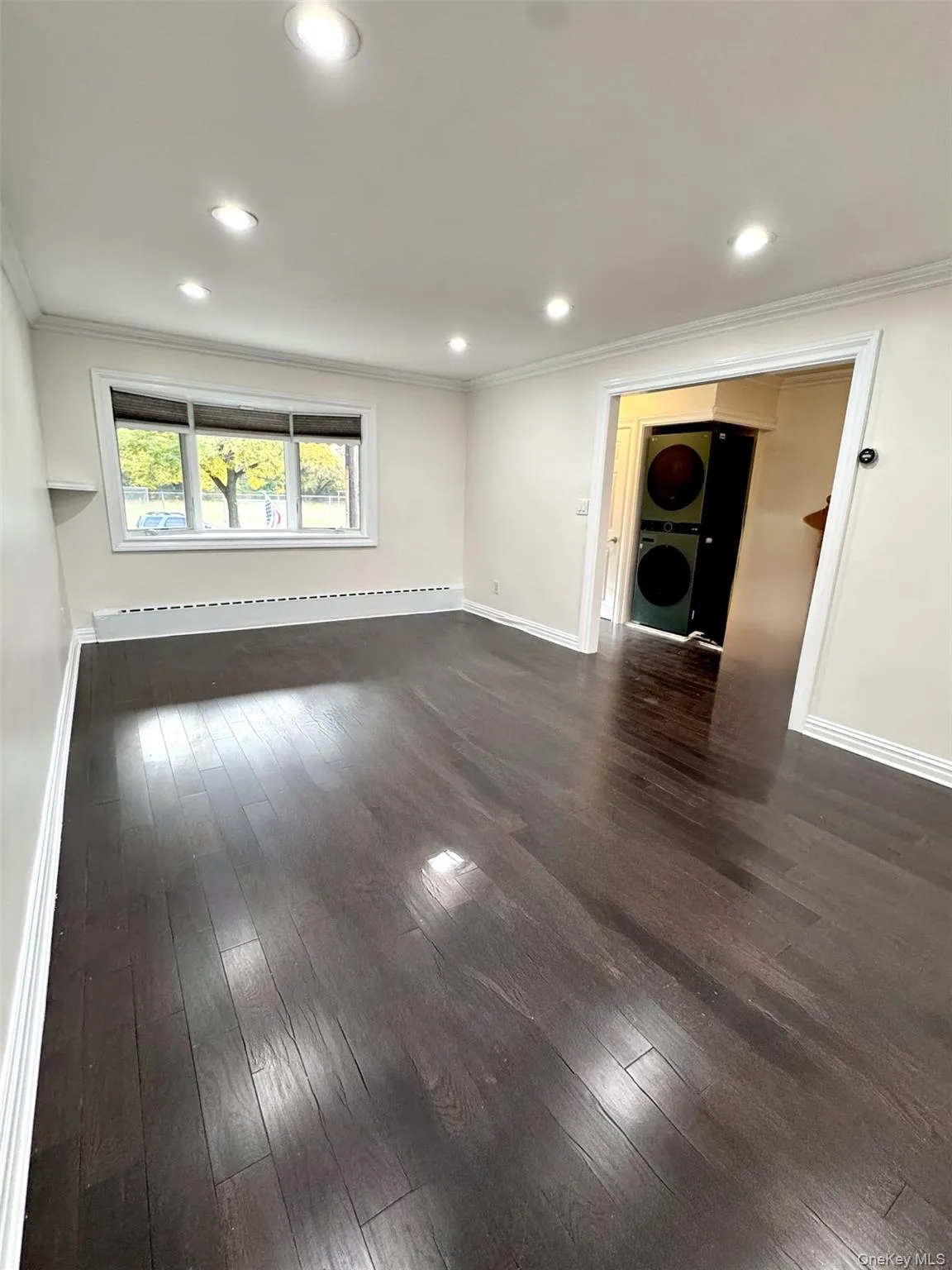 Unfurnished room with dark wood-style floors, ornamental molding, recessed lighting, stacked washer / drying machine, and a baseboard radiator Unfurnished room with dark wood-style floors, ornamental molding, recessed lighting, stacked washer / drying machine, and a baseboard radiator