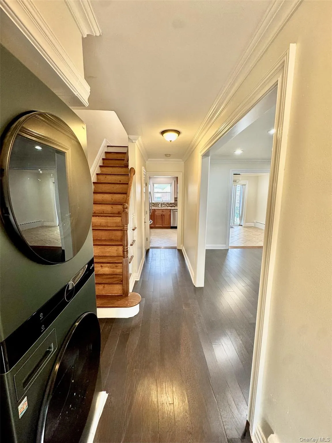 Hallway with dark wood-style floors, crown molding, stairs, and stacked washer / drying machine Hallway with dark wood-style floors, crown molding, stairs, and stacked washer / drying machine