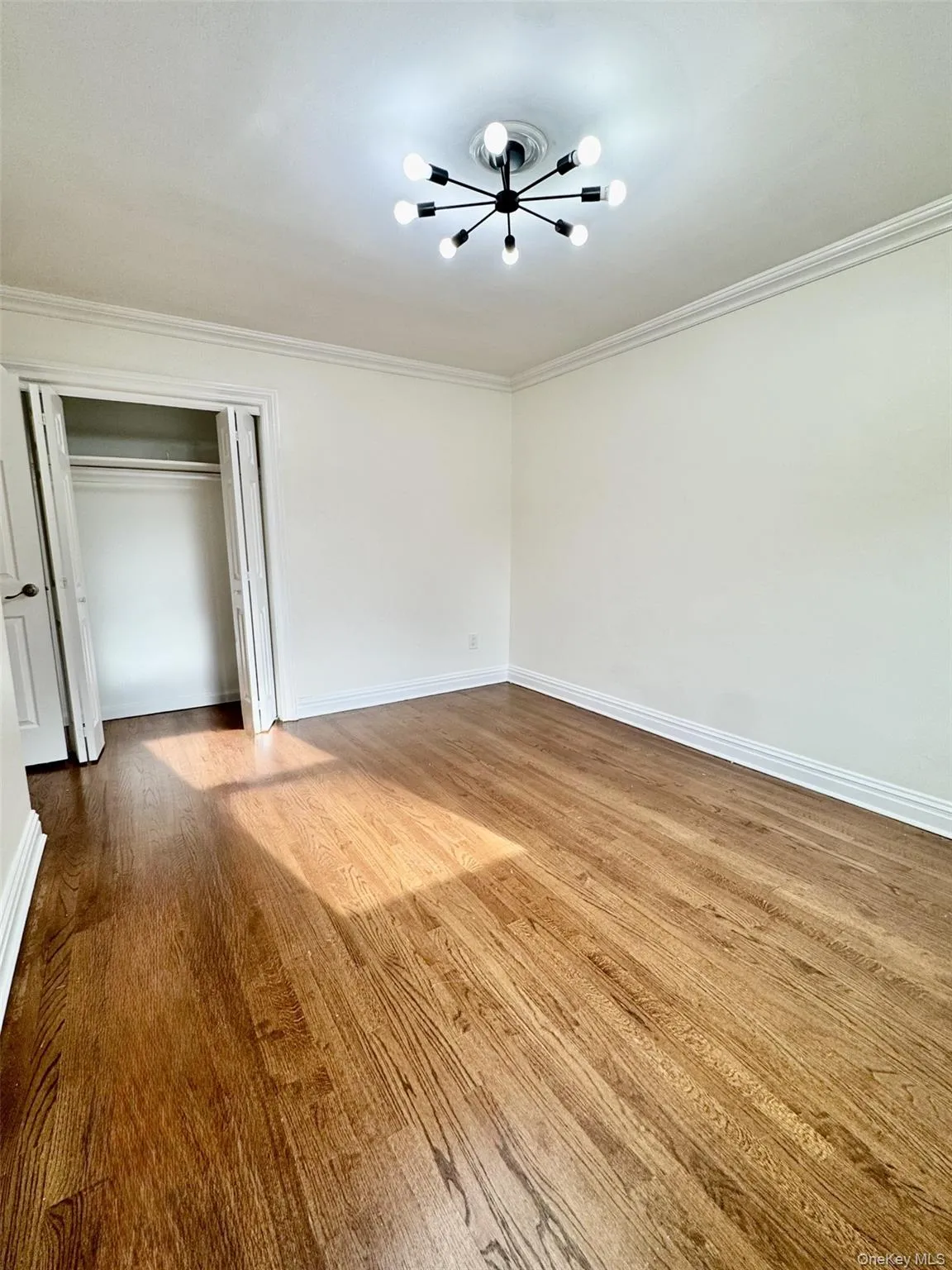 Unfurnished bedroom with a chandelier, a closet, crown molding, and light wood-style flooring Unfurnished bedroom with a chandelier, a closet, crown molding, and light wood-style flooring