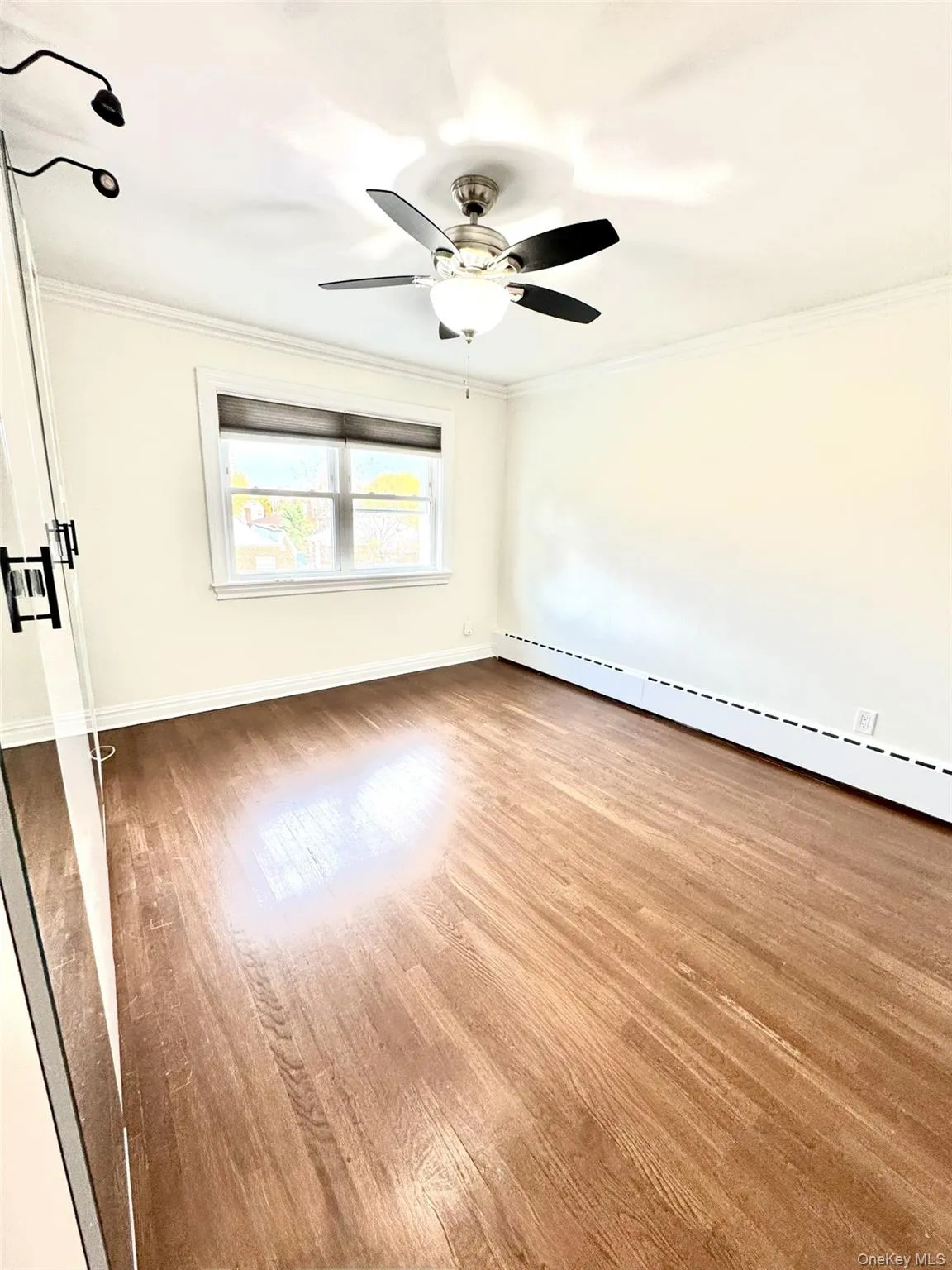 Spare room with baseboard heating, light wood-style floors, and crown molding Spare room with baseboard heating, light wood-style floors, and crown molding