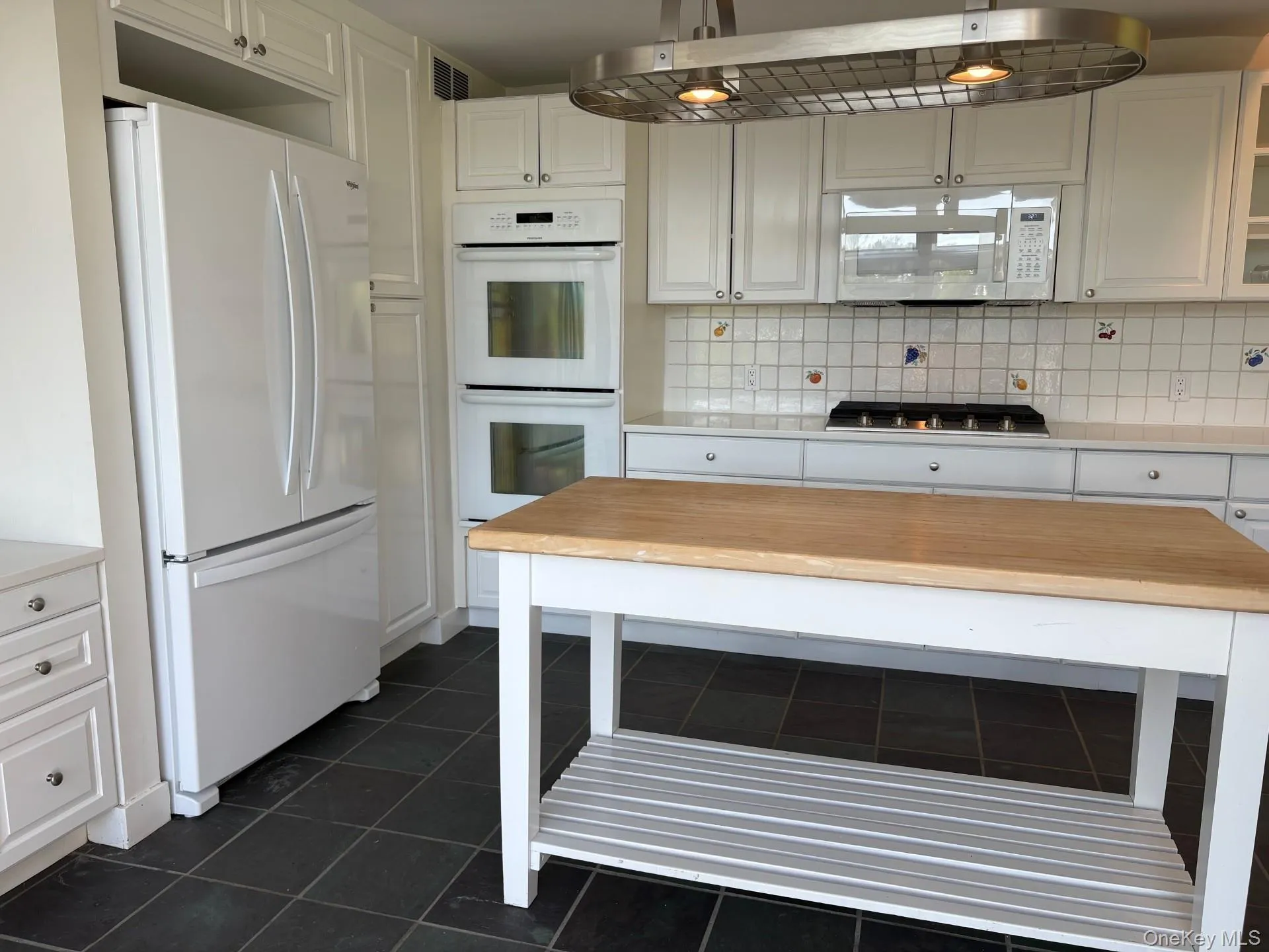Kitchen featuring a butcher block island, white cabinetry, slate tile flooring, and integrated wall ovens Kitchen featuring a butcher block island, white cabinetry, slate tile flooring, and integrated wall ovens