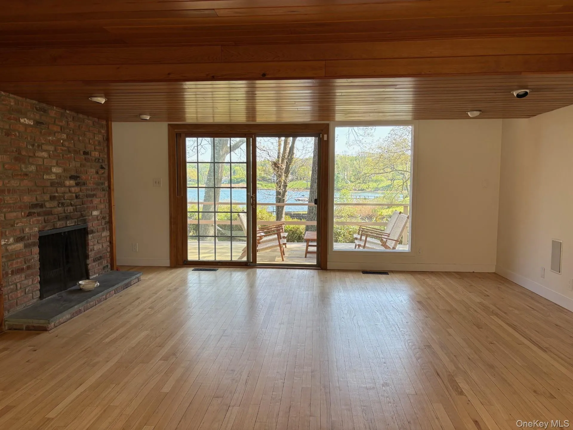 Spacious interior featuring wood-finish flooring, a brick fireplace with a stone hearth, and a wood-paneled ceiling Spacious interior featuring wood-finish flooring, a brick fireplace with a stone hearth, and a wood-paneled ceiling