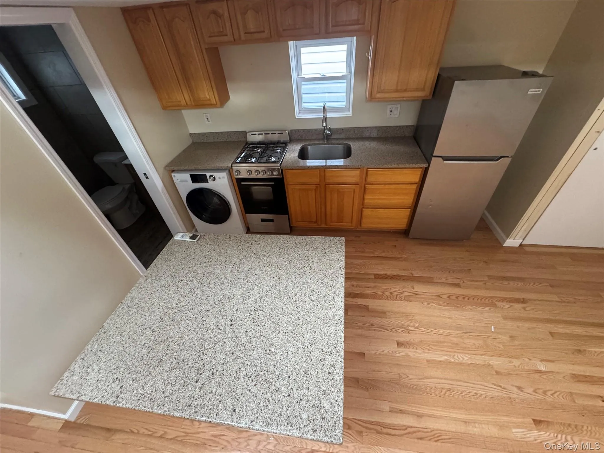Kitchen featuring light wood-type flooring, freestanding refrigerator, brown cabinetry, and stainless steel range with gas stovetop Kitchen featuring light wood-type flooring, freestanding refrigerator, brown cabinetry, and stainless steel range with gas stovetop