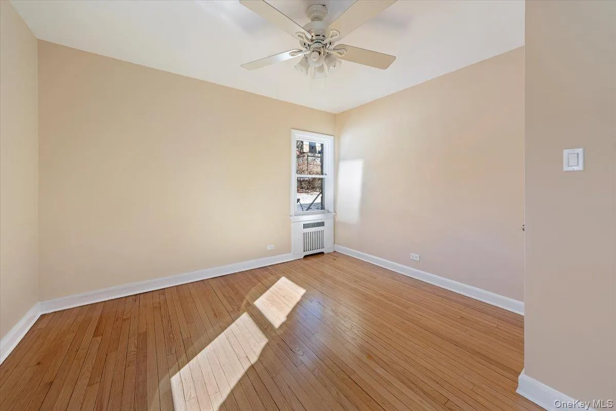 Spare room with light wood-style flooring, baseboards, radiator heating unit, and a ceiling fan Spare room with light wood-style flooring, baseboards, radiator heating unit, and a ceiling fan