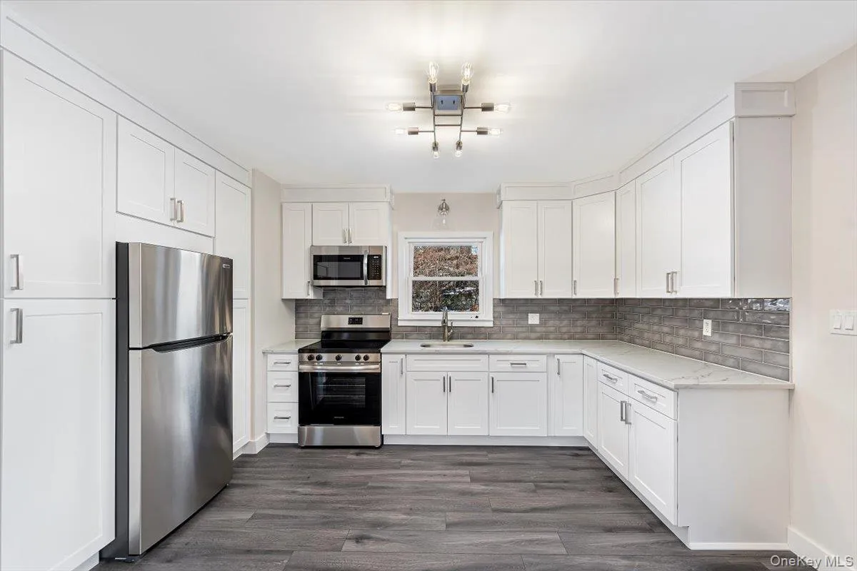 Kitchen with tasteful backsplash, white cabinets, dark wood-style flooring, stainless steel appliances, and a sink Kitchen with tasteful backsplash, white cabinets, dark wood-style flooring, stainless steel appliances, and a sink