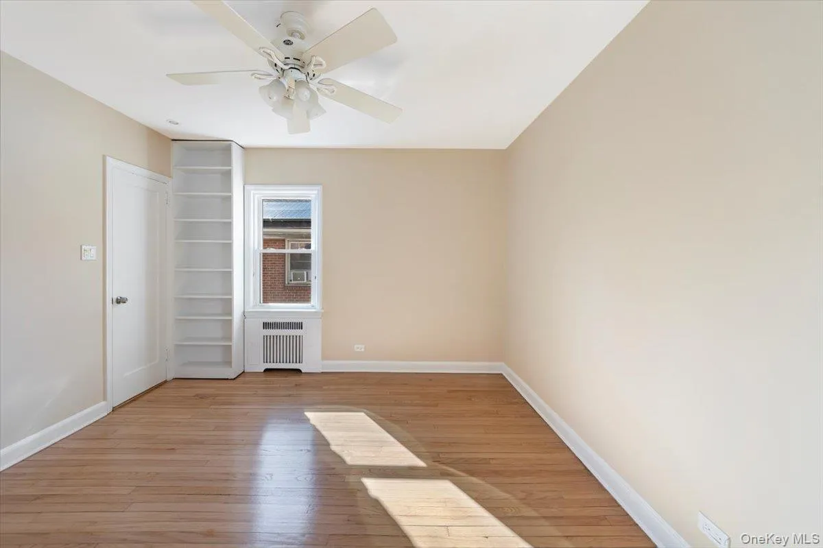 Empty room featuring light wood-style floors, radiator heating unit, baseboards, and ceiling fan Empty room featuring light wood-style floors, radiator heating unit, baseboards, and ceiling fan