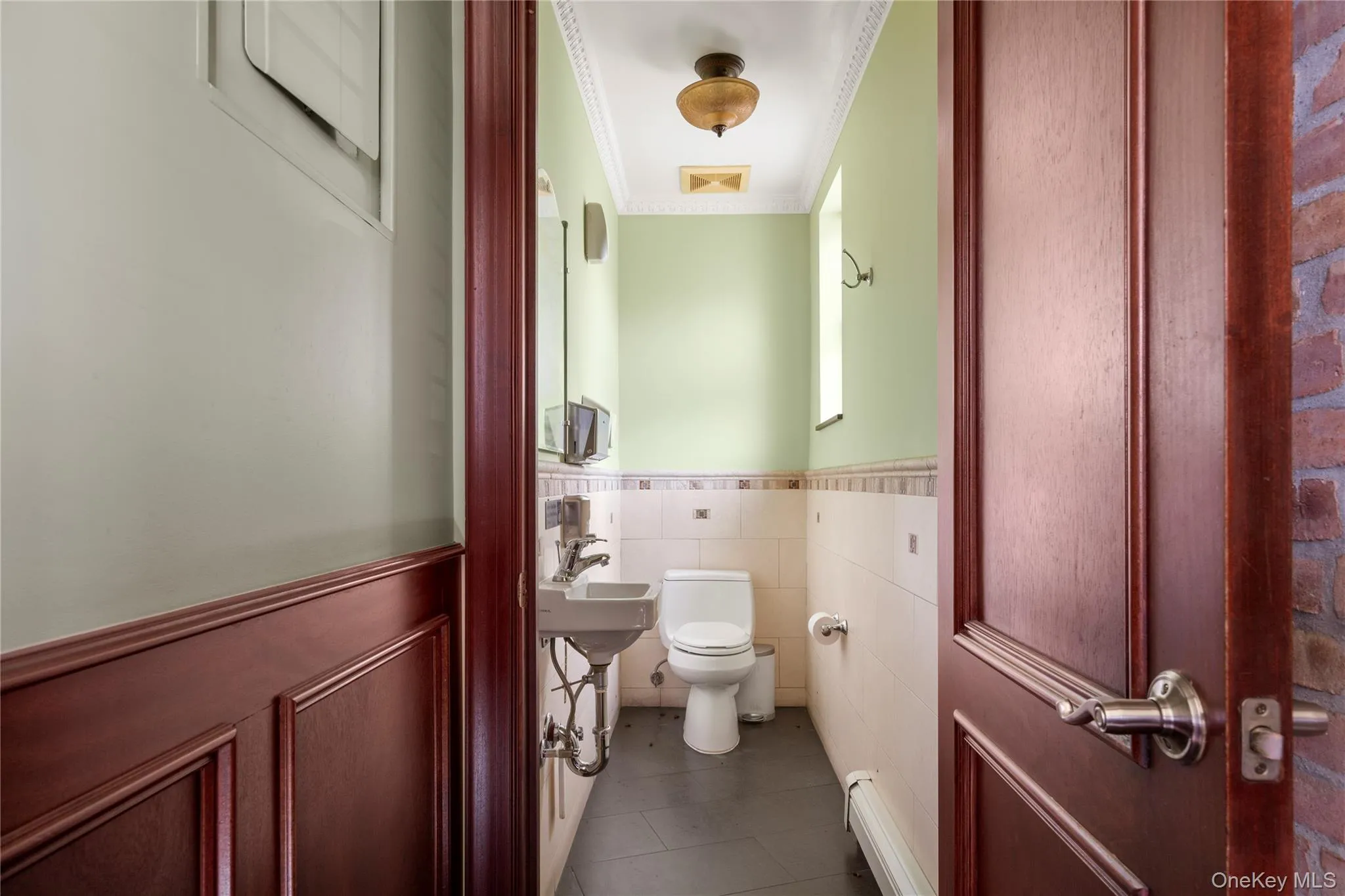 Half bath featuring wainscoting, crown molding, a baseboard radiator, tile patterned flooring, and tile walls Half bath featuring wainscoting, crown molding, a baseboard radiator, tile patterned flooring, and tile walls